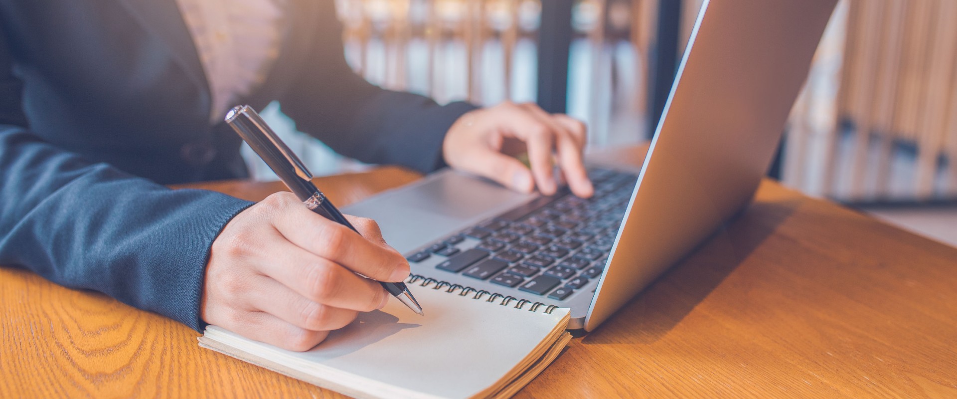 Person writing beside a laptop
